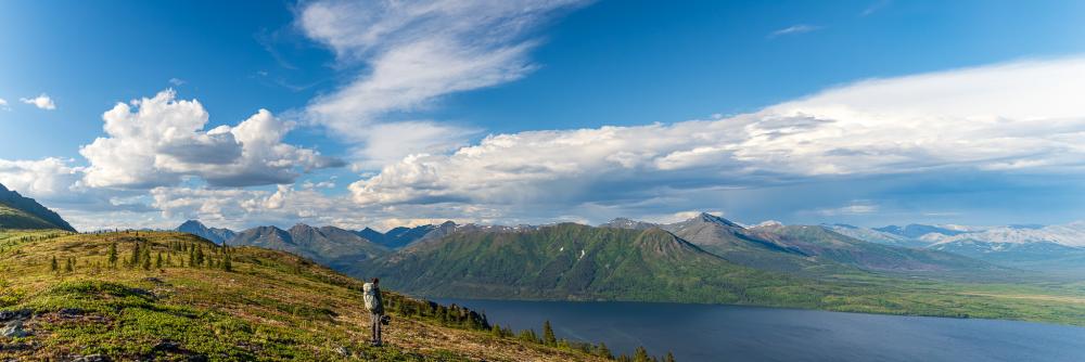 Panoramic view of vast wilderness in Alaska, including a lake and mountain range.