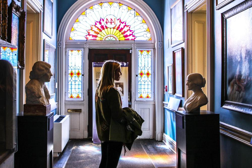 Visitor in a hallway with numerous paintings and busts of suffragists