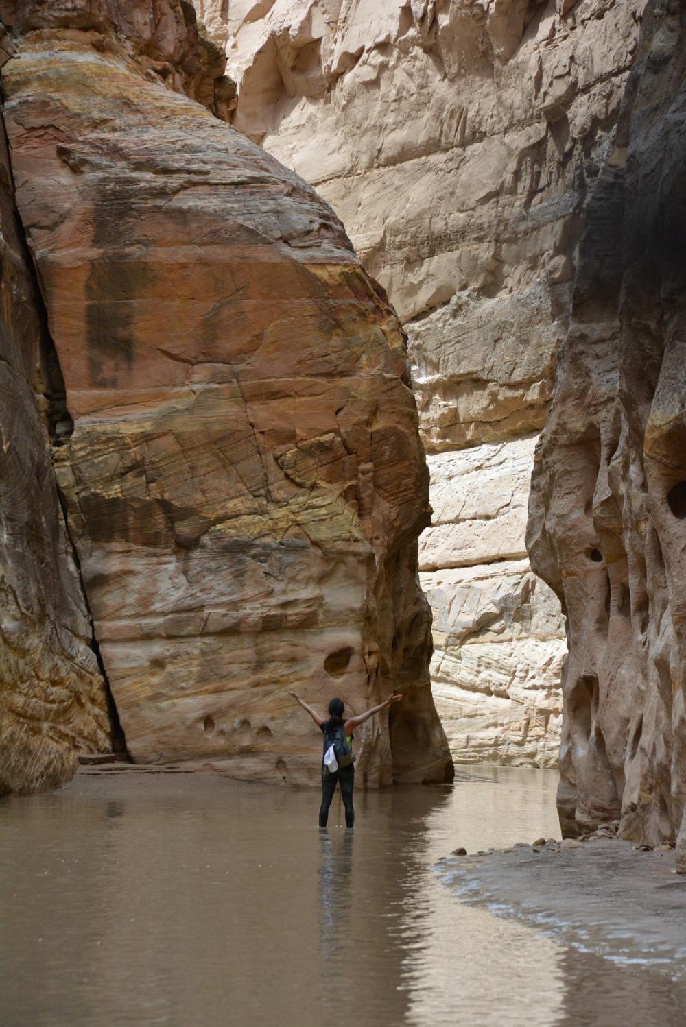 A hiker stands in the middle of a shallow river running through one of Emery County's slot canyons.