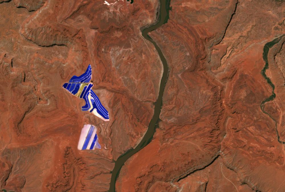 A big blue pond seen from above in the middle of the red desert.