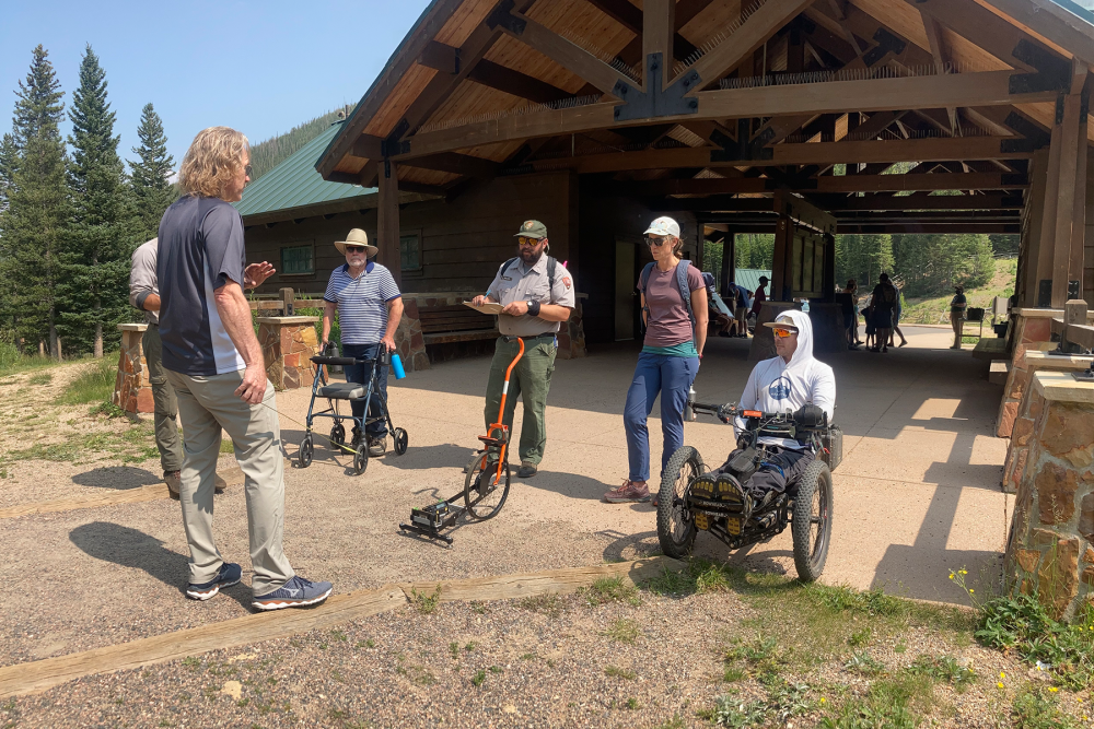 A group of trail staff and an off-road wheelchair learning how to measure a trail with a single wheeled device.