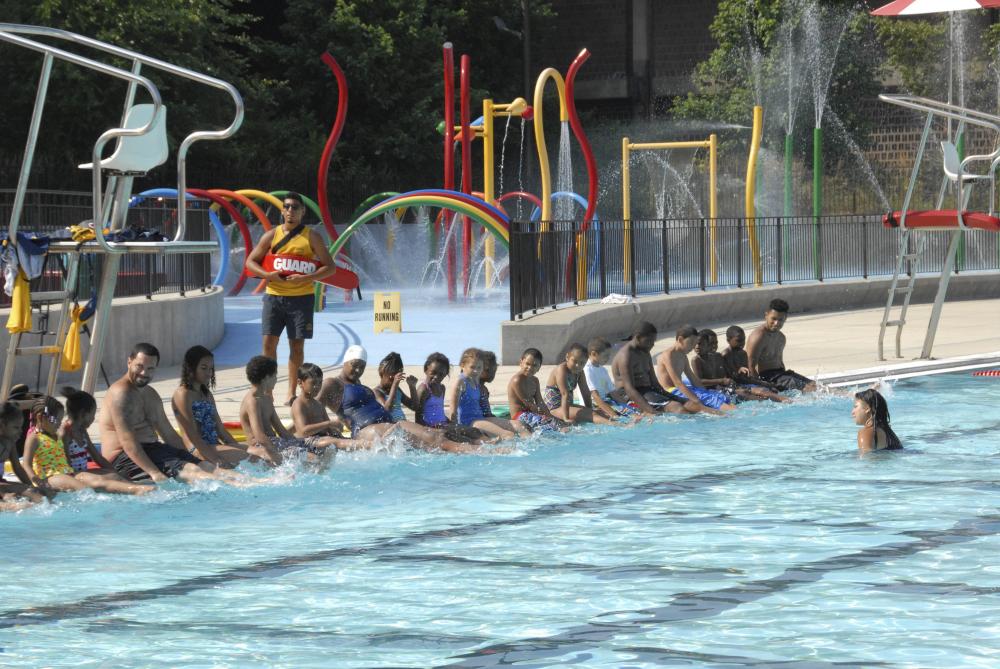 A row of children sit on the edge of a swimming pool at Roberto Clemente State Park in the Bronx, New York