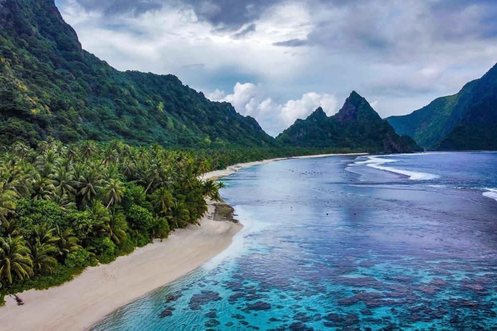 Beach surrounded by tall mountains and greenery. 