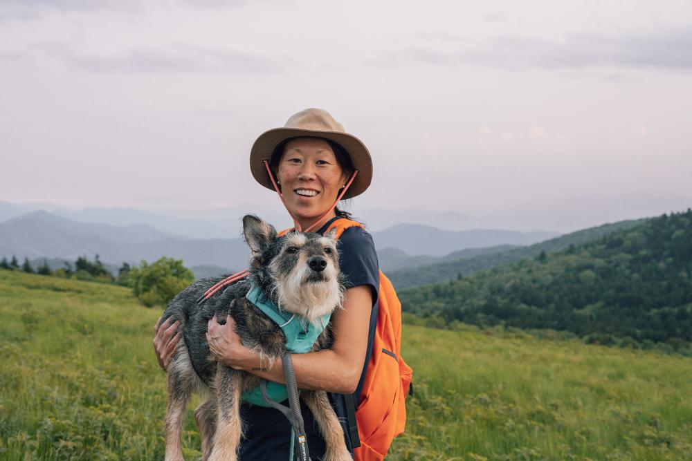woman holding dog surrounding by green landscape