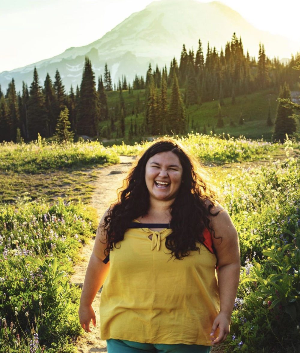 woman smiling with a green field, trees and mountains in the back