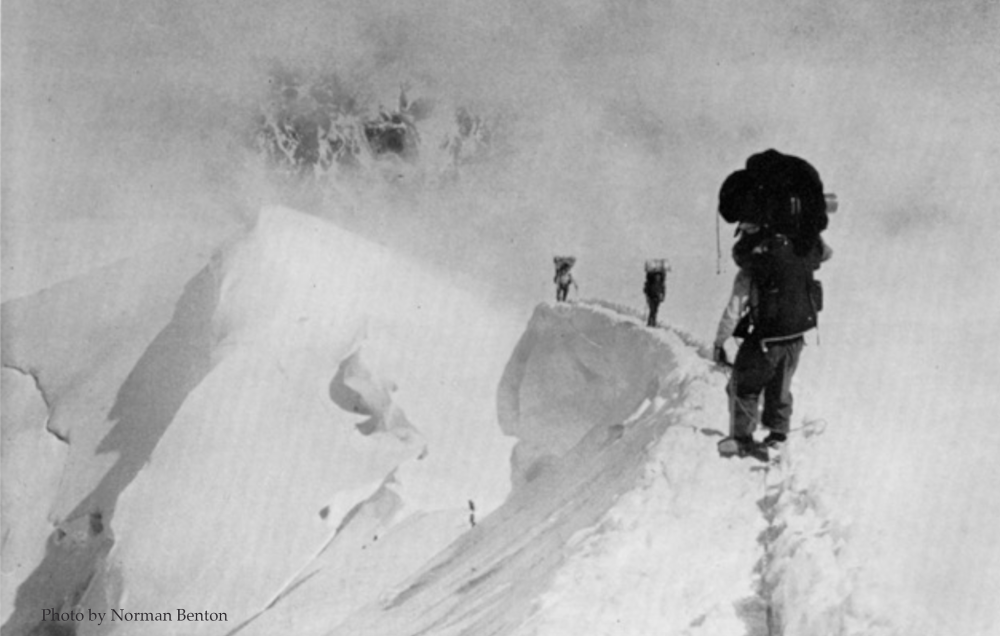 black and white photo of people climbing through snowy mountain