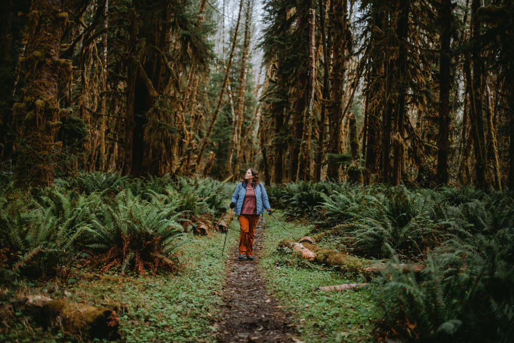 person hiking with their service dog through a forest with tall trees