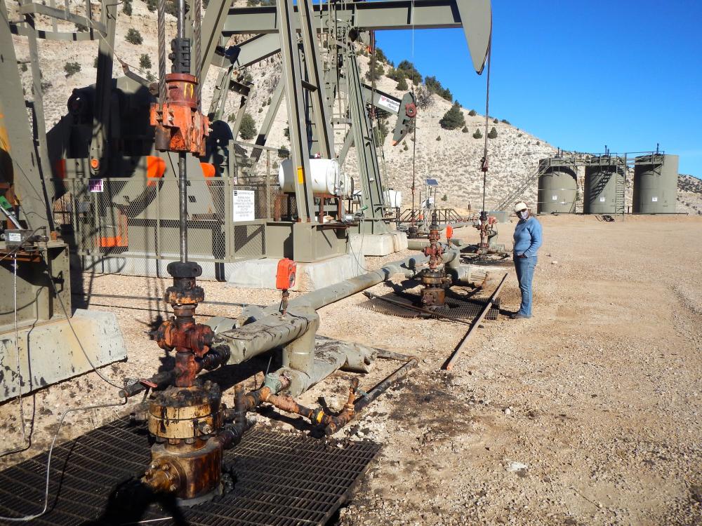 Person in middle distance standing next to oil pump jacks in arid landscape in Ashley National Forest, Utah