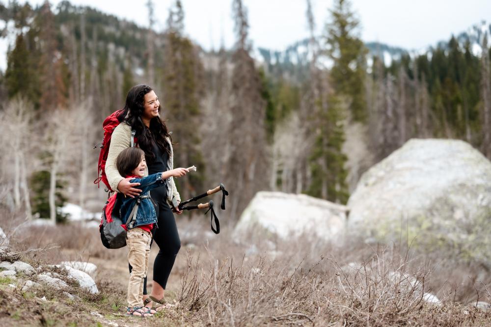 Backpacker stands with child in wooded area.