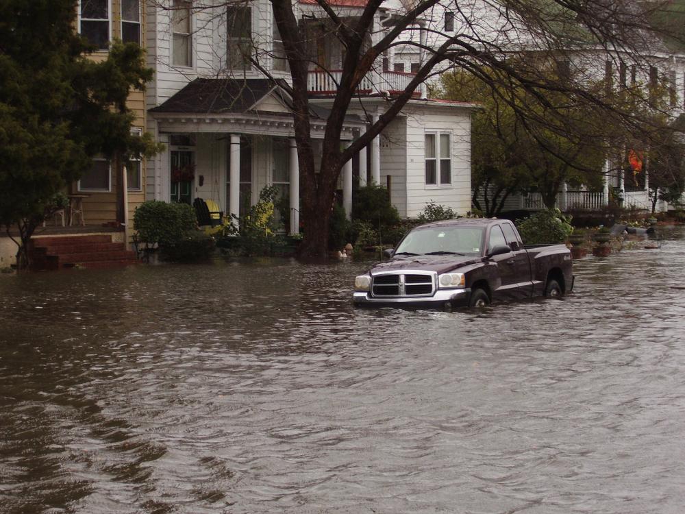 Pickup truck partly submerged in brown flood waters in front of a row of houses