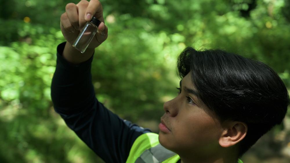 teenager surrounded by trees holding a scientific tube