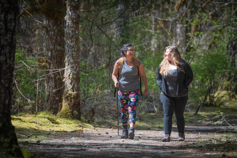 Two women walking side by side on a trail in a forest in Mt. Baker-Snoqualmie National Forest, Washington 