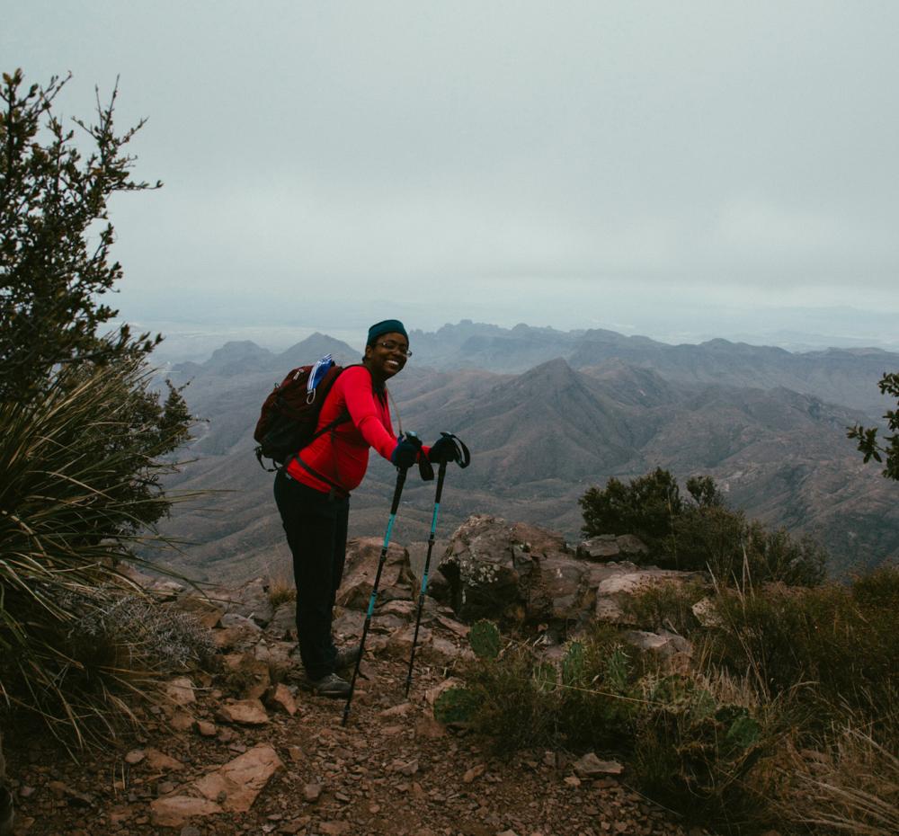 woman with hiking gear, including hiking sticks, looking over a landscape of mountains