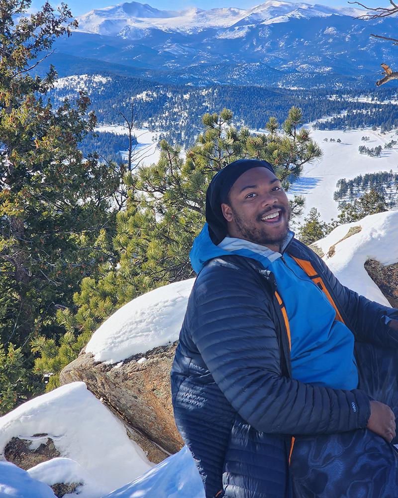 person smiling at camera with mountains and snow in the background