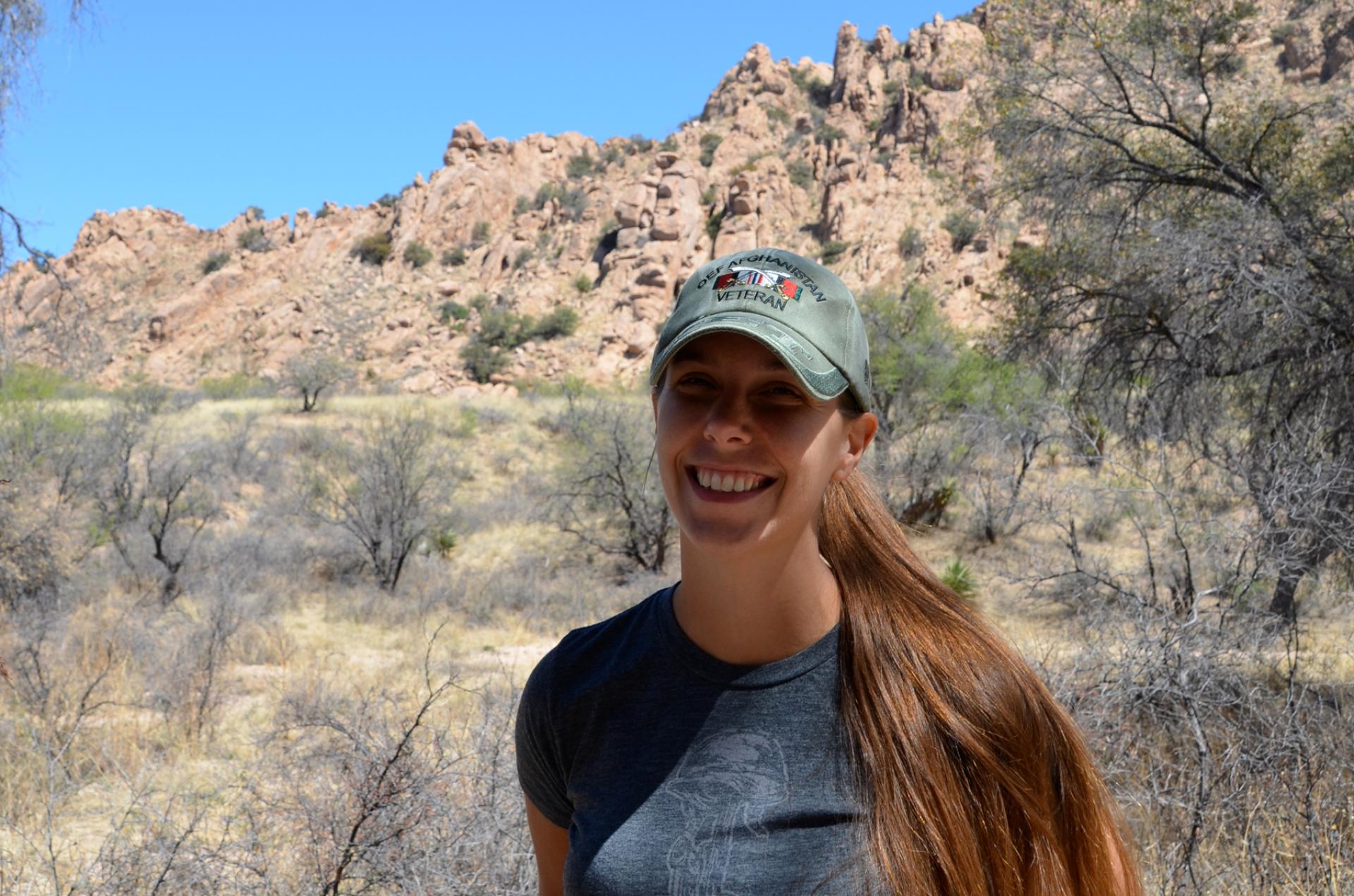 Young woman with baseball cap standing in front of rocky landscape