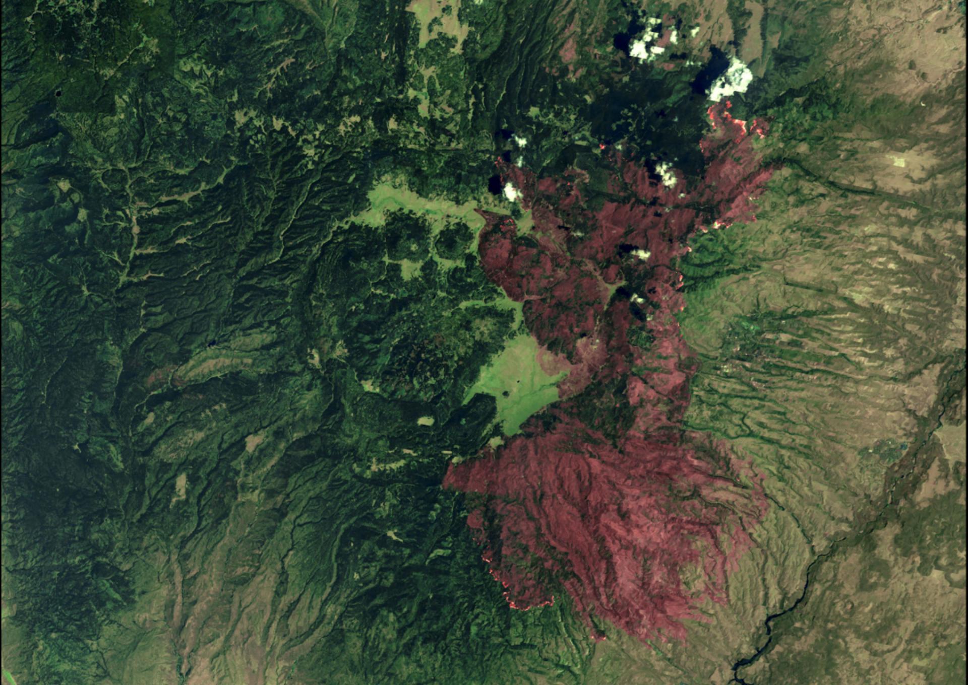 Aerial satellite image of green-tinged terrain showing Santa Fe National Forest on July 2, 2011,  during the Las Conchas Fire. Reddish overlay indicates areas burned