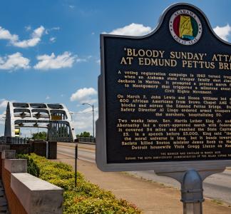 Historic marker with a title that reads "bloody sunday attack on edmund bridge", and a bridge with metal arches in the background