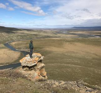 man stands on rock looking at landscape of tundra and a river