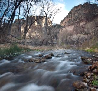 Creek fringed by trees rushes into the distance toward rocky buttes