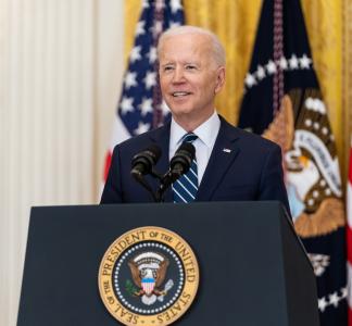 President Joe Biden facing forward, standing behind a lectern with the presidential seal on it and in front of American flags