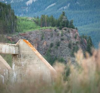 Concrete remains of building with grass in immediate foreground and alpine terrain in background at Camp Hale, Colorado