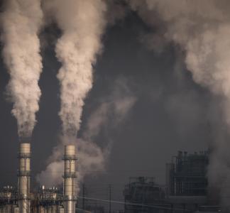 Smoke pouring out of two industrial smokestacks against a gray sky at Cherokee Generating Station