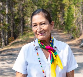 Interior Secretary Deb Haaland smiling in front of a forest.