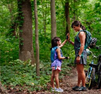 A woman and child high five during a break from bicycling along a forested trail