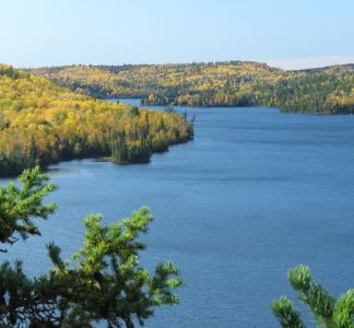 Clear blue lake surrounded by forest-covered hills where the trees are beginning to turn yellow and gold with autumn 