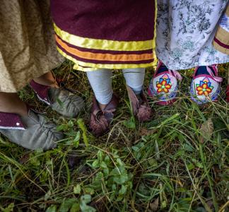 Looking down at the feet of four people wearing traditional Cherokee garments.