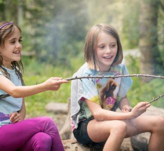Girls cooking hot dogs over a fire while camping