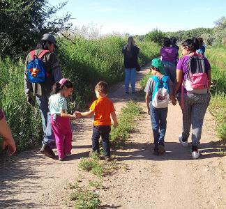 Two small children hold hands with other people while walking down a trail away from the camera