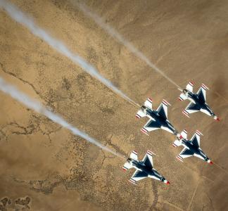 Overhead view of four military-style jets flying above a desert landscape