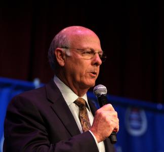 Man speaking into microphone standing in front of blue curtain