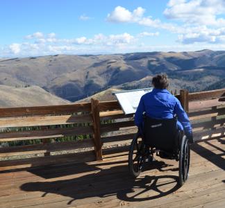 Person on a wheelchair looking over a beautiful scenery of mountains and nature.