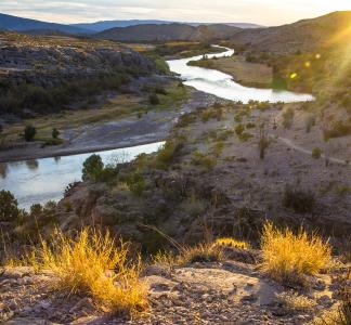 Sunset visible behind mountains and desert landscape with winding river