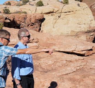 Two men look at something out of frame in front of a red-rock desert landscape in Moab, Utah