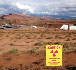 Sign reads "CAUTION - contamination area" in foreground of industrial site at the Moab Uranium Mill Tailings Remedial Action (UMTRA) project in Moab, Utah