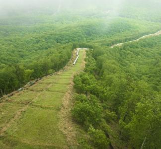 Aerial view of pipeline components lined up on verdant hillside near forests with fog in background