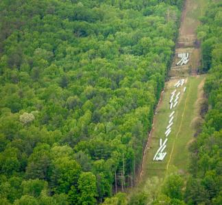 Aerial view of pipeline components lined up on verdant hillside on path cut through forest 