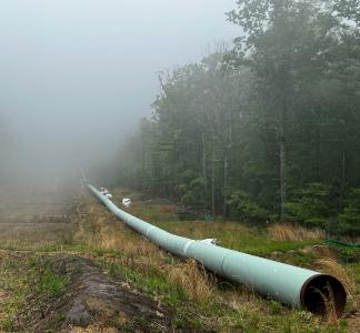 Under-construction pipeline receding into foggy distance with trees running alongside it