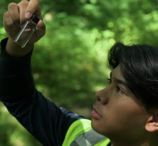 teenager surrounded by trees holding a scientific tube