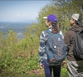 Two hikers in green park looking out at water view.