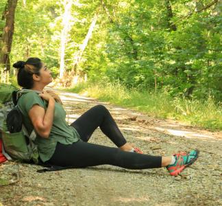 Person with backpack sitting on side of dirt trail in wooded area 