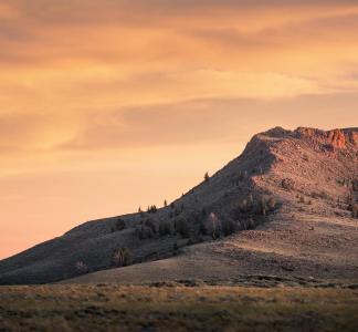 Butte rising above field with orange-tinted clouds in the background, Northern Red Desert, Wyoming
