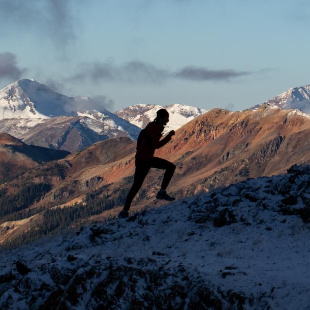 A person running up a ridge with mountains in the background.