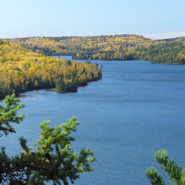 Clear blue lake surrounded by forest-covered hills where the trees are beginning to turn yellow and gold with autumn 