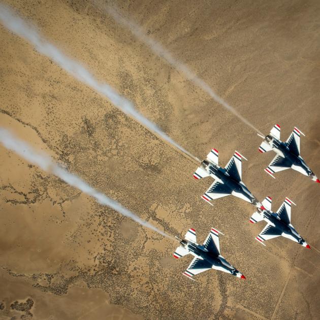Overhead view of four military-style jets flying above a desert landscape