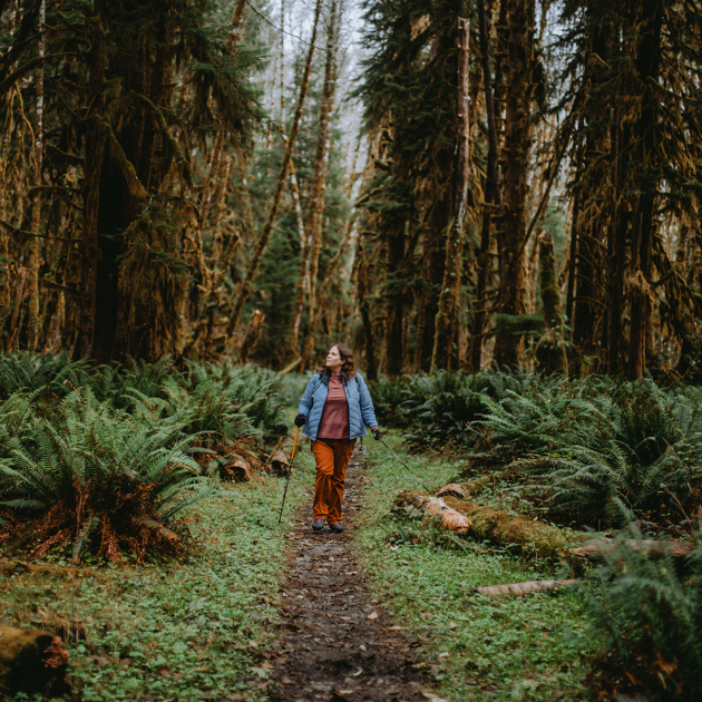 person hiking with their service dog through a forest with tall trees