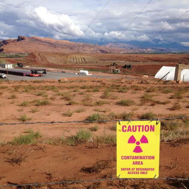 Sign reads "CAUTION - contamination area" in foreground of industrial site at the Moab Uranium Mill Tailings Remedial Action (UMTRA) project in Moab, Utah